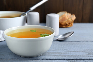 Delicious chicken bouillon with parsley on grey wooden table. Space for text