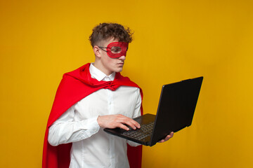 guy in a superhero costume uses a laptop on a yellow background, an employee superman types on a...