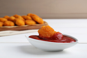 Tasty chicken nugget with ketchup on white wooden table, closeup