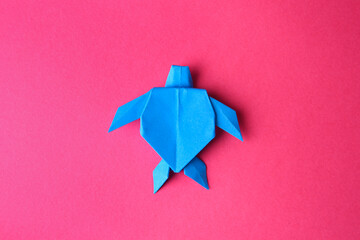Origami art. Handmade light blue paper turtle on pink background, top view