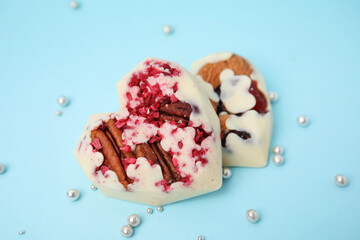 Tasty chocolate heart shaped candies with nuts on light blue background, closeup