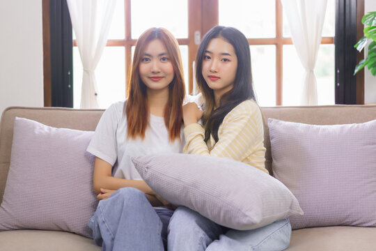 Relax at home concept, LGBT lesbian couple sitting on couch and looking at camera to taking photo
