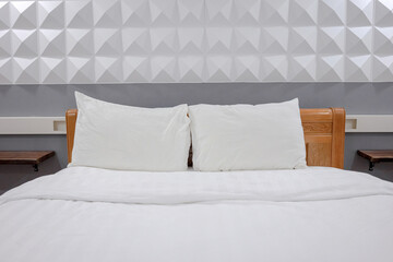 View of a bed with a white duvet cover and two pillows in front of a gray wall. An empty bed ready to go to sleep.