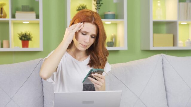Young woman looking at phone thoughtful, in trouble, confused.
Young woman looking at phone at home unhappily looking at phone anxiously, in trouble.

