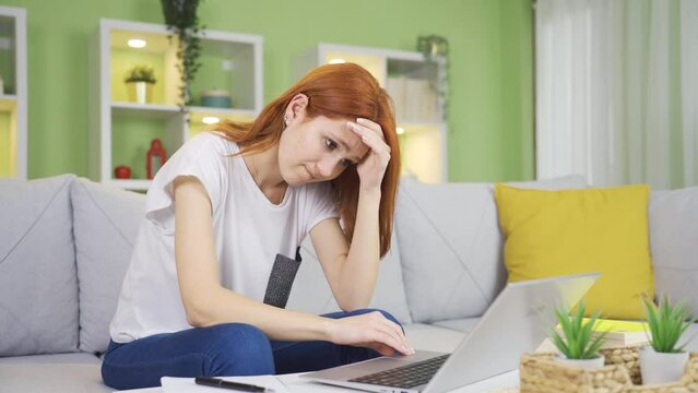Young woman working on laptop thoughtful, in trouble, confused.
Young woman looking at laptop unhappy at home worriedly working on laptop, in trouble.
