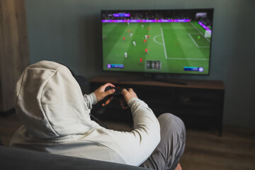Guy playing a video game console. Game is football. Back view. Selective focus