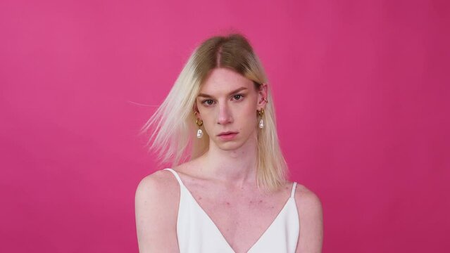 Portrait close up of young transvestite man in a dress on a pink background