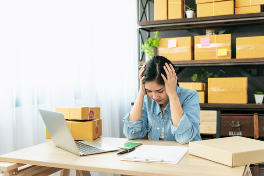 Desperate Asian woman stress headache depressed from startup small business at home office. Failure business woman work at home office. Online seller entrepreneur has problem delivery unhappy job