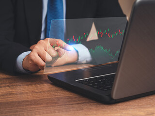 Hand of a businessman pointing at graph stock on a virtual screen while sitting at the table in the office
