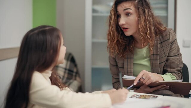 Woman Psychologist communicates with a girl in the office. The child draws and talks with the doctor.