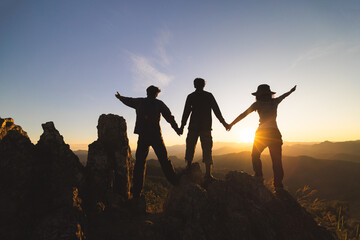 Silhuette Young group praying on the mountain, arms outstretched observing a beautiful dramatic sunrise.