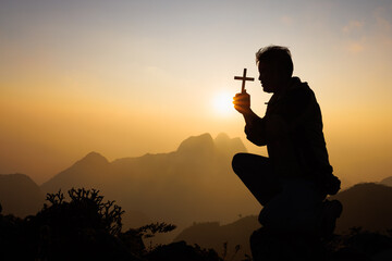 Silhouette of christian man hand praying, man holding a crucifix praying, spirituality and...