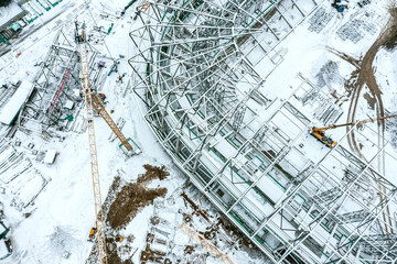 aerial top view of snow-covered building site with yellow crane. new stadium under construction.