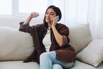 Obraz premium Woman blogger with phone lying at home and talking on the phone on sofa with laptop and working freelancer online, smiling with teeth