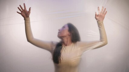 A young woman is trying to break through the plastic. The concept of pollution of the planet with plastic.