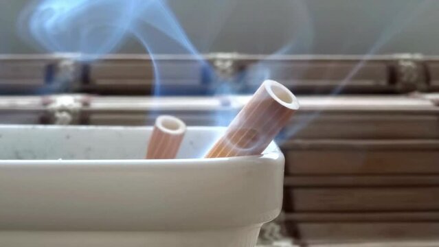 Cigarette burning in Ashtray Filled With Cigarette Butts closeup shot lifestyle healthy concept