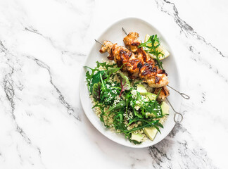 Delicious lunch - chicken bacon skewers and couscous, avocado, arugula salad on a light background top view