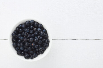 Fresh raw Patagonian Calafate berries (lat. Berberis heterophylla), photographed overhead on white wood with copy space on the side (Selective Focus, Focus on the berries)