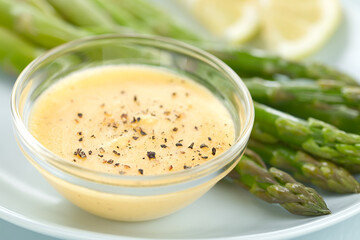 Hollandaise sauce with freshly ground black pepper served in glass bowl, green asparagus and lemon...
