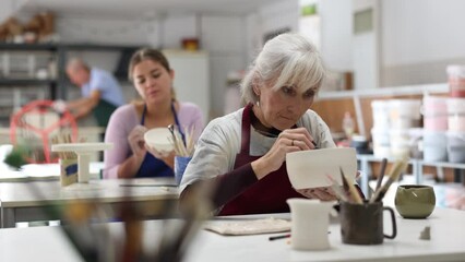 Woman potter with paintbrush, painting on plate in workshop, working in pottery studio