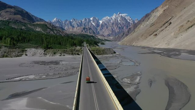 Aerial view following an auto rickshaw crossing a bridge in the scenic mountains of the Hunza Valley.