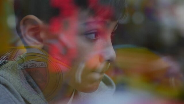 Unique view through the glass of a boy's face while he plays arcade games with the lights flickering on his face.