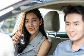 Happy Asian young woman showing remote car looking at camera in vehicle at automotive rental, customer satisfied feedback, test driving, dealership or purchasing concept