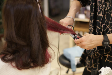 女性の髪にヘアアイロンをかける男性美容師