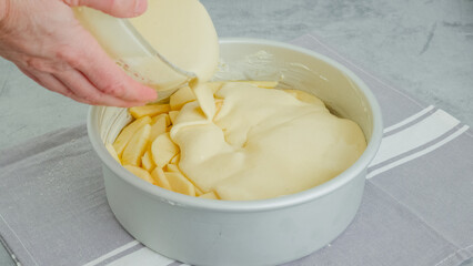 Chef pouring cake batter into a baking pan on the top of apple slices. Apple cake preparation...