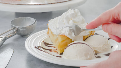 Eating a fruit cake. Slice of a freshly baked apple cake with whipped cream topping, served with vanilla ice cream and chocolate close-up on a white plate on a kitchen table
