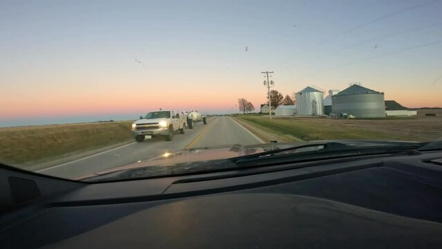 Point of view while driving on a rural county highway; farm house, barn, grain bins and empty fields are visible; rural Midwest at sunrise in the winter