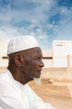 Old African Man Sitting In Front Of His House, Profile View, Serious Expression, Celebration Clothing And Hat, Eighty Years Old, Photo