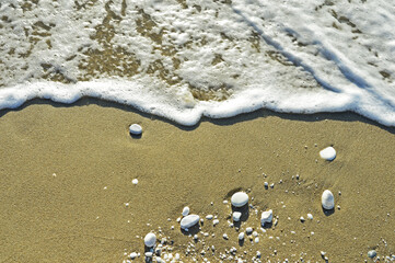 Sea foam and white pebbles of different sizes on the wet sand on