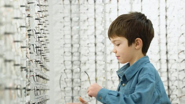 Little boy in optics store choosing glasses. Ophthalmology family concept
