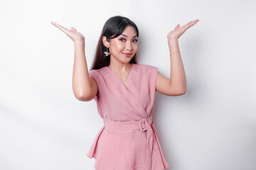 Excited Asian woman dressed in pink, pointing at the copy space on top of her, isolated by white background