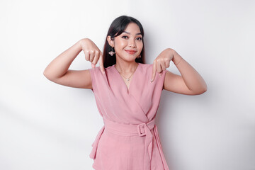 Excited Asian woman dressed in pink, pointing down at the copy space, isolated by white background