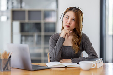 Young adult happy smiling Hispanic Asian student wearing headphones Online education using laptop in university campus or at virtual office. College female student learning remotely.