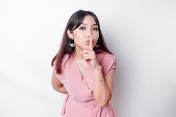 Portrait of a young Asian woman tell be quiet, shushing with serious face, hush with finger pressed to lips, isolated by white background