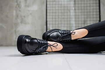 Female slender legs in black leggings and black leather loafers close-up. Women's spring-summer...