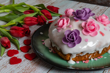 Heart-shaped cake with lemon icing decorated with pink and purple flowers.