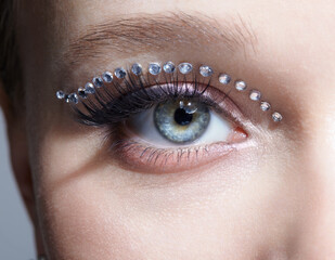 Closeup macro shot of human female eye with unusual makeup. Woman with rhinestones arrows on eyelid.