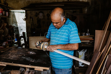 hispanic senior man carpenter using sandpaper on a polished wood in workshop in Mexico Latin America