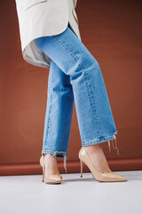 Close-up of female legs in blue jeans and fancy beige high heels. Women's leather pumps.