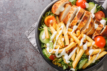 Pittsburgh steak salad consist a lettuce salad with cheese, chicken breast, French fries, and ranch dressing on top closeup on the bowl on the table. Horizontal top view from above