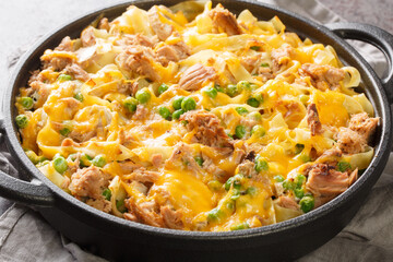 Homemade Tuna casserole with pasta, green peas, mushrooms and cheddar cheese close-up in a frying pan on the table. Horizontal
