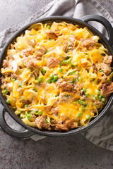 Tuna casserole with noodles, green peas, mushrooms and cheddar cheese close-up in a baking dish on the table. Vertical top view from above