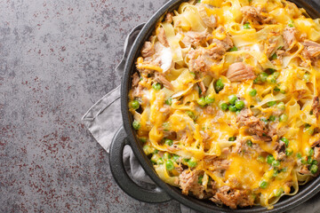 Homemade Tuna casserole with pasta, green peas, mushrooms and cheddar cheese close-up in a frying pan on the table. Horizontal top view from above