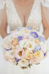 Vertical photo of bridal bouquet with seasonal flowers in white, ivory and purple colors at weding ceremony 