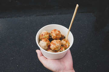 Close-up view of hand holding a delicious fried meatballs in a white bowl, thai street food from Thailand.