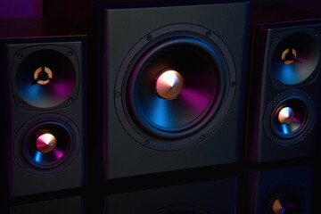 Two sound speakers and subwoofer on dark background with neon lights. Set for listening music. Acoustic equipment